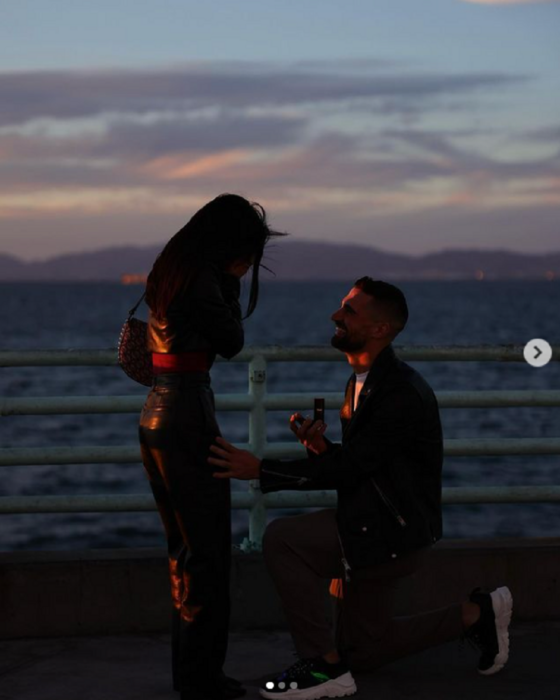 Becky G y Sebastian Lletget en una imagen donde el futbolista le está pidiendo matrimonio a la cantante en una bella puesta de sol