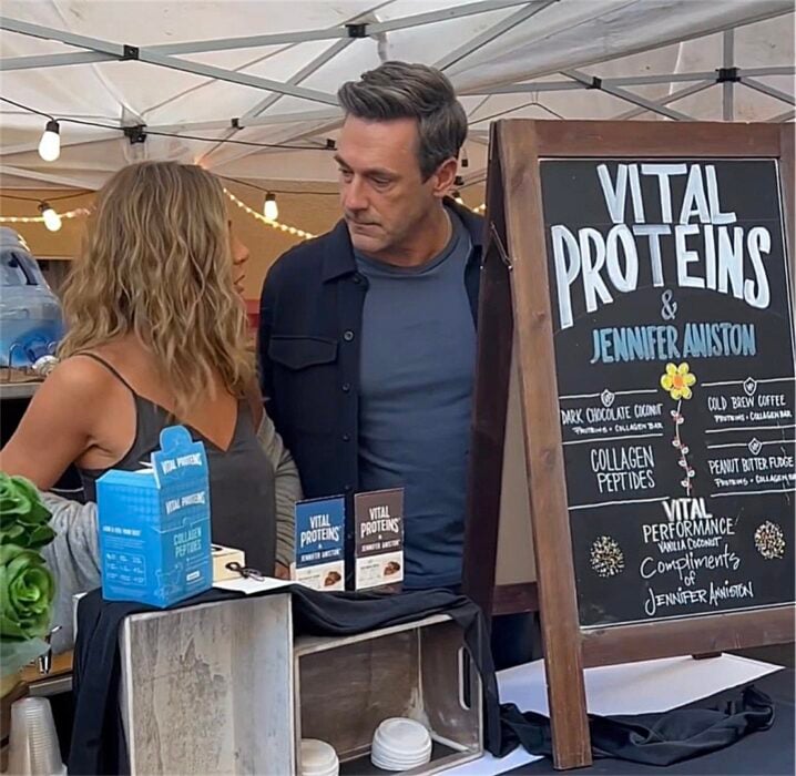 Jennifer Aniston junto al actor Jon Hamm en un puesto de venta de barras de proteína 