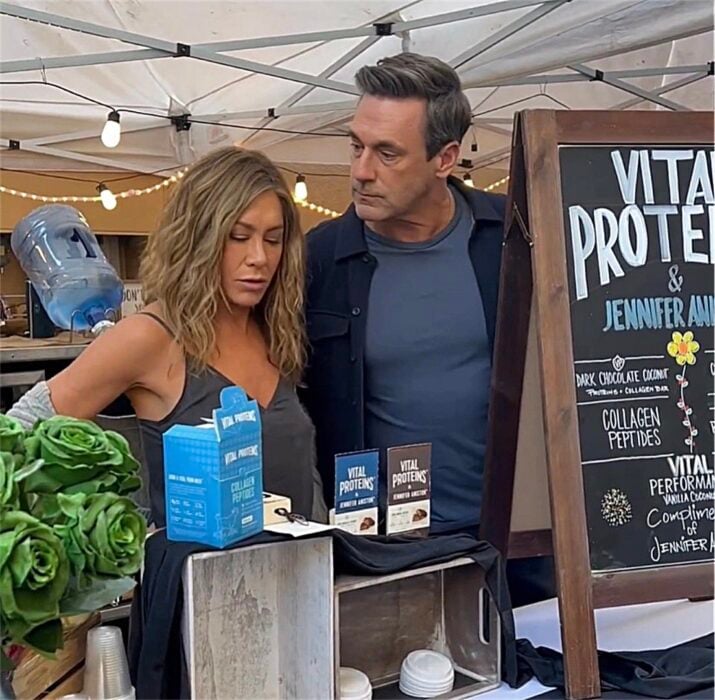 Jennifer Aniston junto al actor Jon Hamm en un puesto en el set de grabación de The Morning Show ofreciendo sus barras de proteína