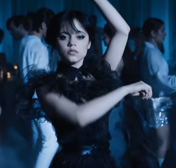 Jenna Ortega en la escena del baile de la escena de Merlina la nueva serie de Netflix lleva un vestido negro y tiene los brazos en movimiento