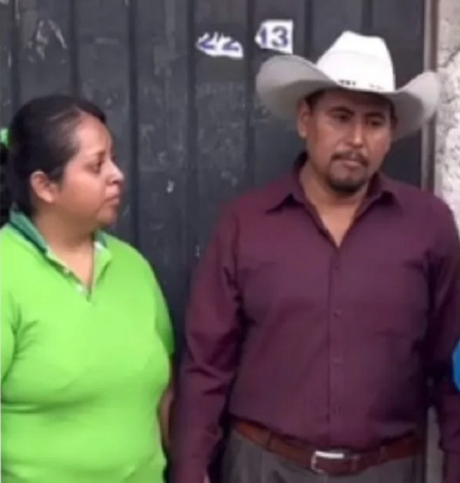 una pareja de novios mexicanos él lleva sombrero blanco con camisa guinda ella trae el cabello recogido con una trenza alta y una playera verde está afuera de una casa
