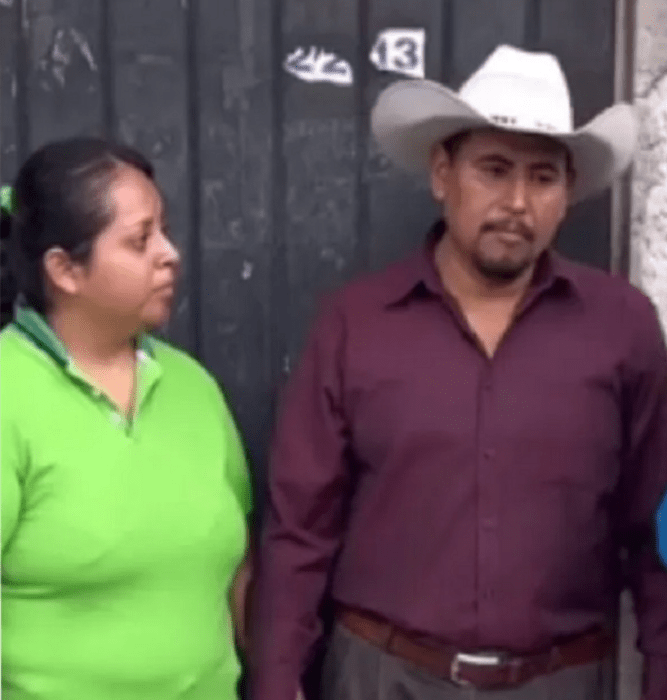 una pareja de novios mexicanos él lleva sombrero blanco con camisa guinda ella trae el cabello recogido con una trenza alta y una playera verde está afuera de una casa