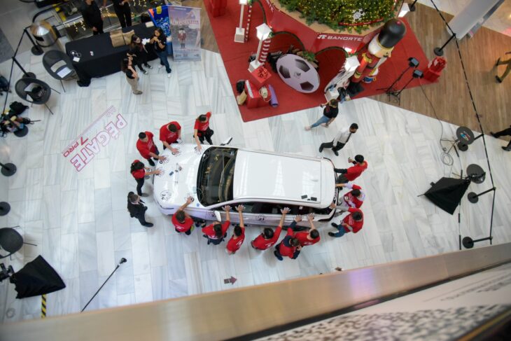 fotografía que muestra a muchas personas en un centro comercial con la mano sobre una camioneta que será sorteada para quien dure más tiempo con la mano sobre ella 