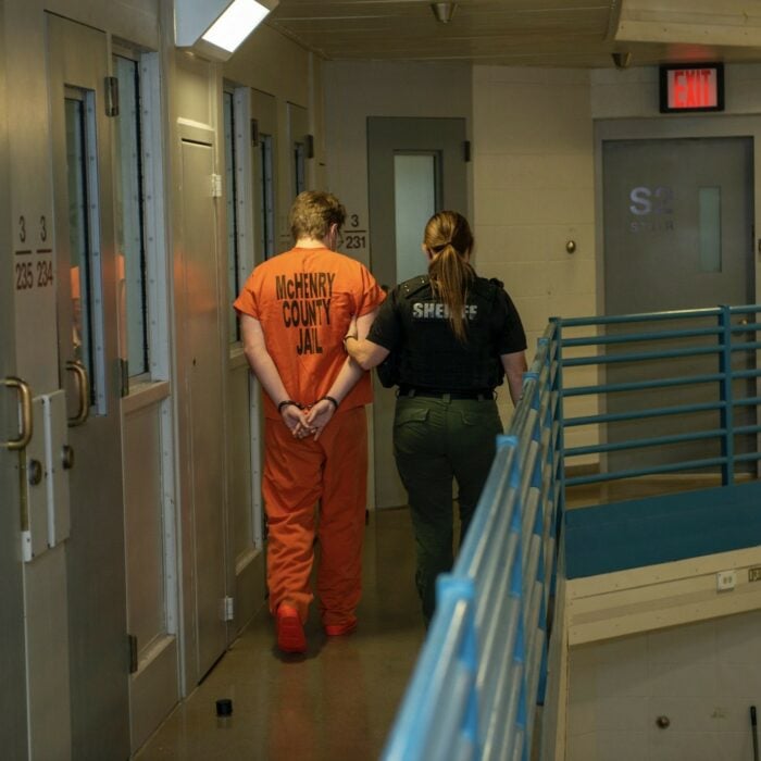 Mujer oficial llevando del brazo a preso esposado dentro de una prisión 