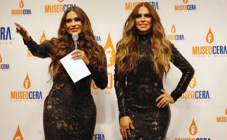 Galilea Montijo feliz junto a su figura de cera llevan un vestido negro de noche el cabello largo suelto peinado con ondas la conductora trae un micrófono y lleva algunas notas en unas tarjetas blancas 