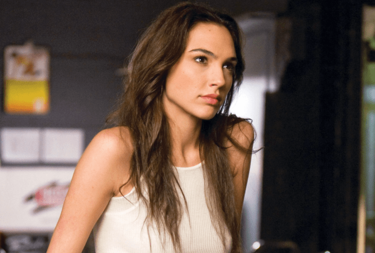 Gal Gadot en una escena de Rápido y furioso lleva una playera sin mangas blanca y trae el cabello largo y suelto su maquillaje es discreto