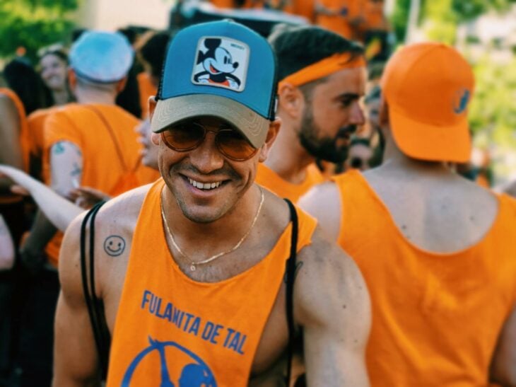 fotografía del actor Mario Casas vestido en color naranja con una gorra de Mickey Mouse en una marcha del orgullo gay