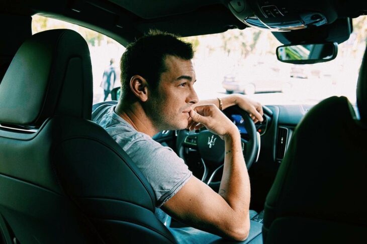 Mario Casas arriba de un carro volteando hacia la ventana del copiloto con la mano en la boca 