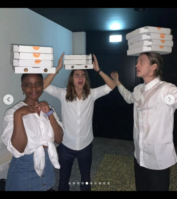 tres actores del elenco de Merlina con cajas de pizza sobre su cabeza 