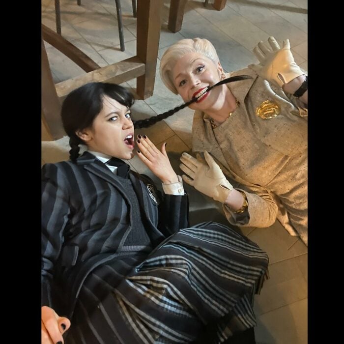 fotografía de Jenna Ortega caracterizada como Merlina siendo mordida de una trenza por parte de la actriz Gwendoline Christie en su papel como la directora Larissa Weems en Nunca Más