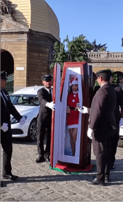 image of a Santa Claus coming out of a coffin surrounded by men in chauffeur uniforms 