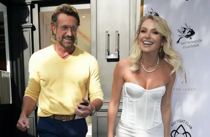 Gabriel Soto e Irina Baeva caminando juntos ambos estan sonriendo ella lleva un corsé blanco y el cabello rubio suelto tare un collar de perlas en el cuello el trae un camisa tipo sudadera amarilla y lleva pantalón negro