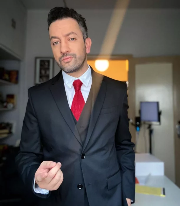 imagen del comediante y youtuber Chumel Torres lleva un traje negro con corbata roja y camisa blanca el cabello lo trae corto y tiene una sombra de barba y bigote