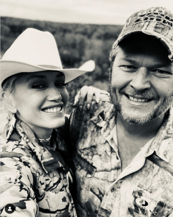 Gwen Stefani y su esposo posando en una fotografía blanco y negro ella lleva un sombrero de campo y él una gorra ambos usan chaquetas tipo militares