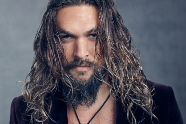 Jason Momoa posa para la cámara con mirada penetrante lleva el cabello ondulado largo y suelto 