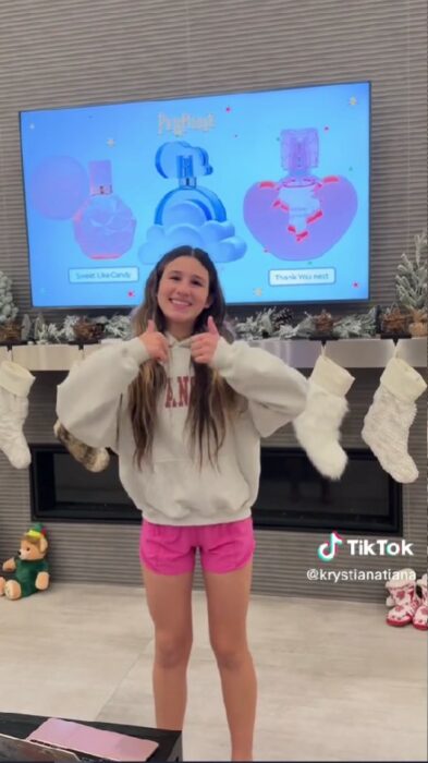 chica posando feliz frente al televisor de la sala después de exponer a sus papás lo regalos que quiere para Navidad