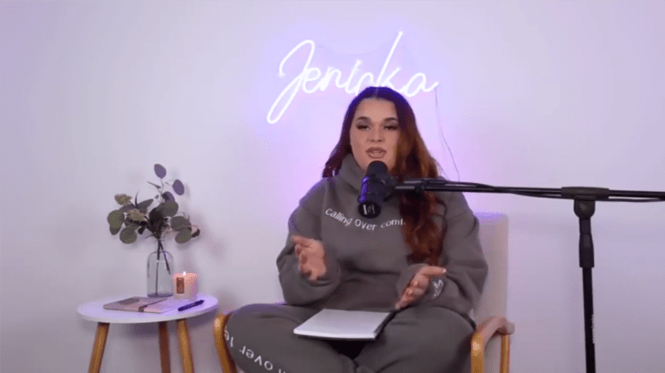 Jenicka López the fourth daughter of Jenni Rivera image from her Overcomfort podcast the girl is wearing comfortable clothes she is speaking in front of a microphone some lights with her name are on behind her