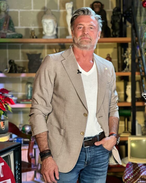 Photograph of Argentine actor Juan Soler posing with a sand-colored jacket to match denim jeans 