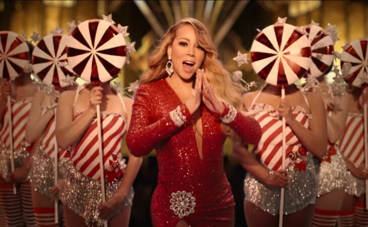 la cantante Mariah Carey interpretando su éxito de Navidad All i want for Christmas is you lleva un vestido de noche rojo y esta acompañada por abilarinas que sostienen paletas en colores rojo y blanco