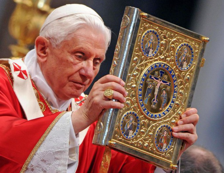 el papa emérito Benedicto XVI sostiene un libro sagrado en una ceremonia religiosa viste ornamentos de color rojo
