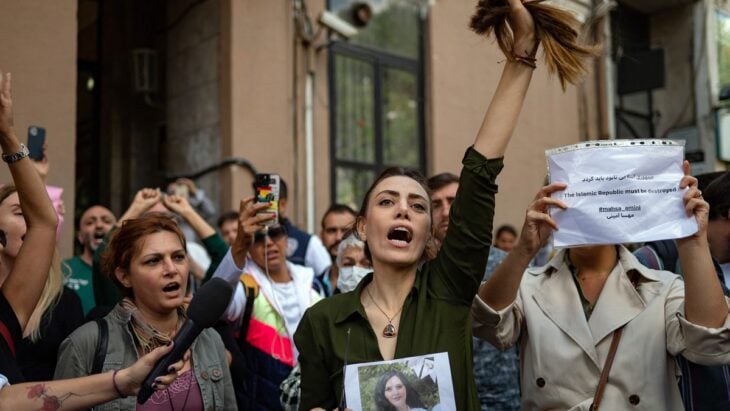 grupo de manifestantes iraníes toman las calles de la capital del país una mujer lleva la foto Masha Amini y sostiene los mechones del cabello que se corto ella misma en la mano