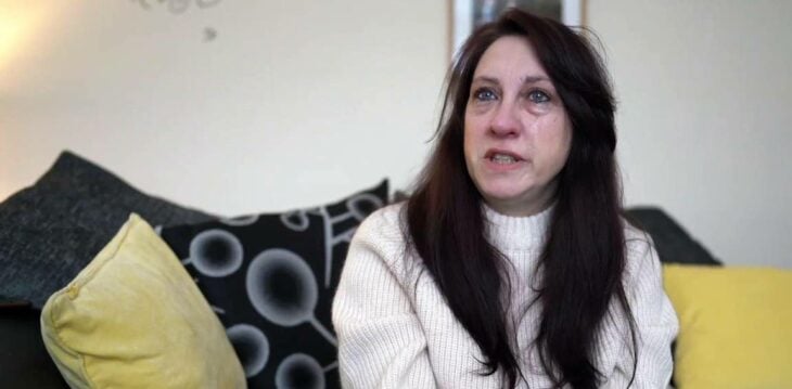 mujer llora al relatar su historia está sentada en la sala de su casa lleva un suéter crema y poco maquillaje
