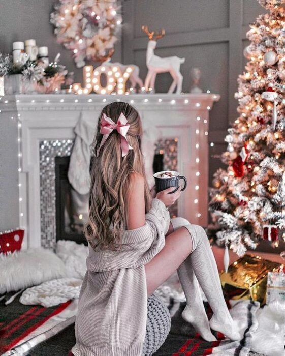 Mujer posando frente a árbol de navidad y decoraciones