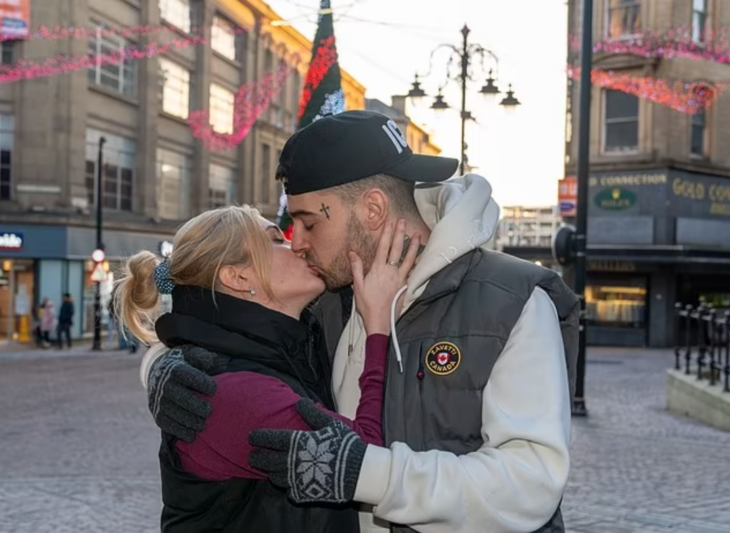 una pareja se besa en una plaza de Inglaterra ambos llevan ropa de invierno informal