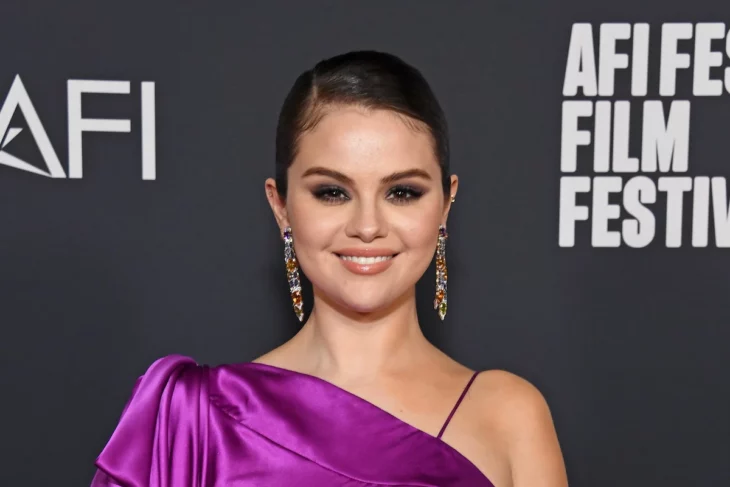 la cantante Selena Gomez posando en una alfombra roja lleva un vestido de noche fucsia el cabello recogido y unos aretes dorados muy largos su maquillaje es de noche