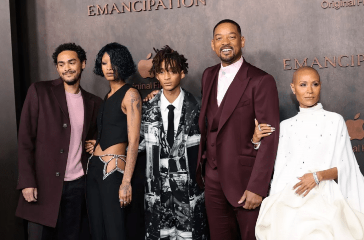 Will Smith acompañado de su esposa Jada Pinkett Smith, su hija Willow y sus dos hijos Trey y Jaden en la alfombra roja de Emancipación el actor lleva un traje guinda y su esposa luce un vestido blanco y elegante sus hijos visten mas casuales