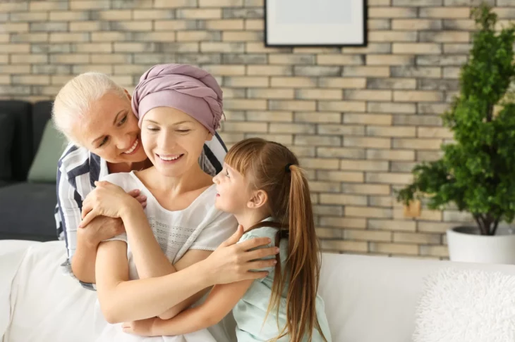 Mujer con cáncer sentada su mamá y su hija abrazándola