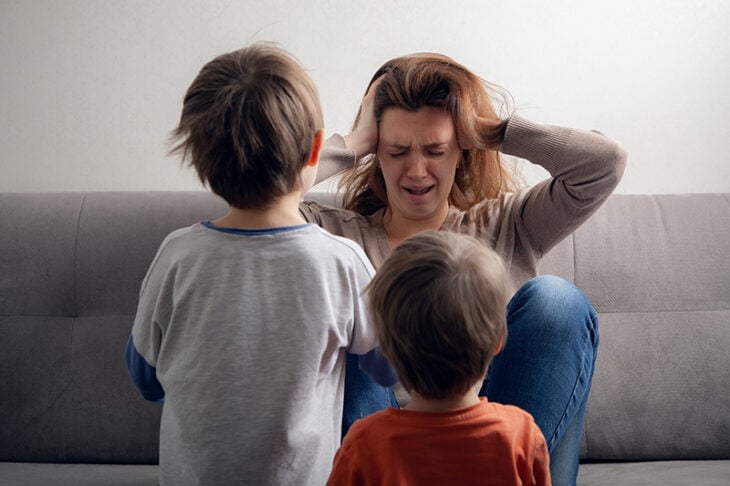 Mujer impaciente con sus hijos agarrándose la cabeza y dos niños de espalda