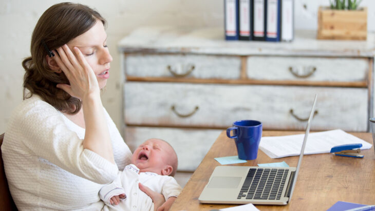 Woman sitting with baby crying stressed clutching her head