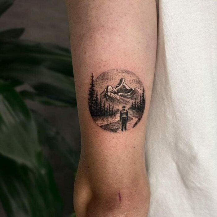 Arm with round tattoo of man in the mountains
