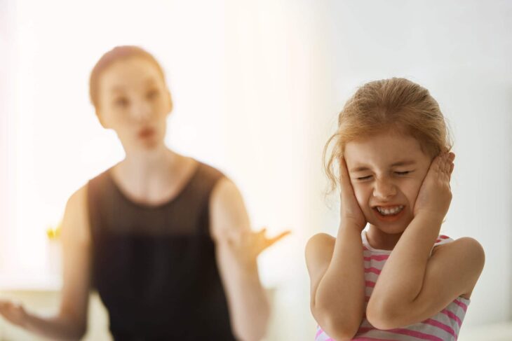 Mamá regañando a su hija mientras ella se tapa las oídos con las manos 