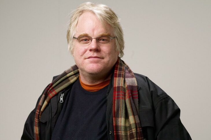 Philip Seymour Hoffman posando para la cámara lleva una bufanda de cuadros y ropa informal oscura