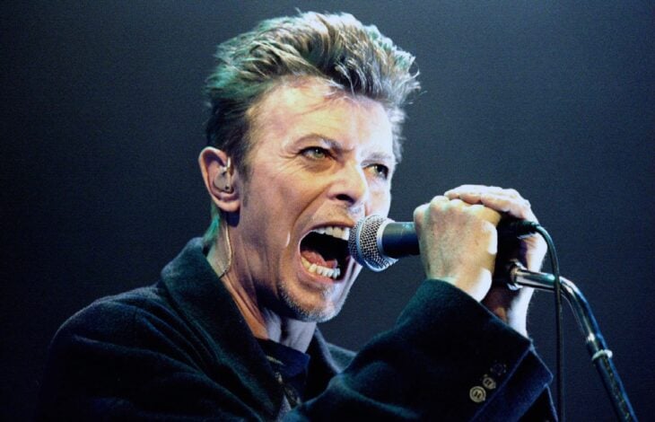 David Bowie está en el escenario cantando una canción viste saco negro
