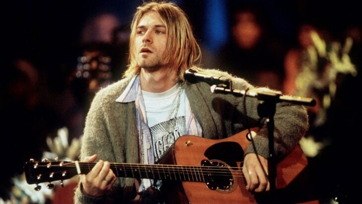 Kurt Cobain in a live performance carries his guitar on his lap and casual clothing