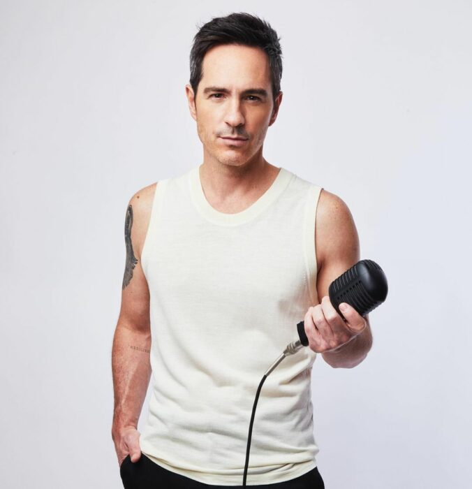 Mauricio Ochmann con playera blanca y micrófono en la mano