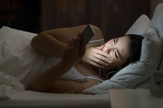 mujer acostada en la cama viendo el celular 