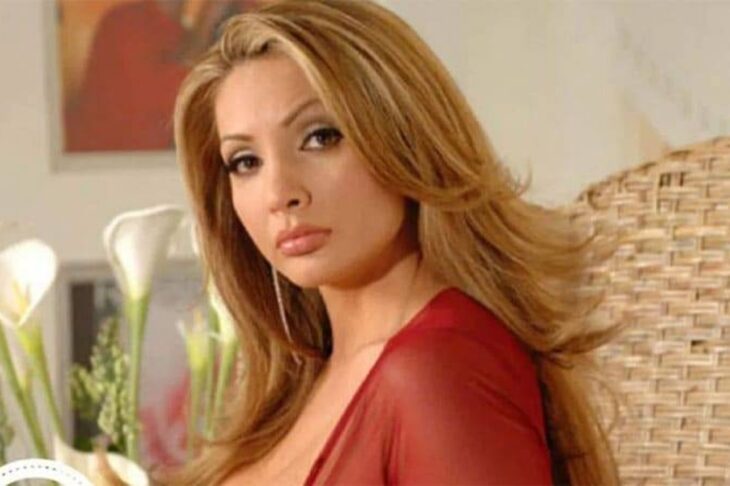 The actress Paty Navidad in an image where she is looking at the camera wears a red dress with a neckline, her hair is loosely combed in waves in a blonde tone, her makeup is marked