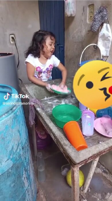 screenshot of a girl washing dishes in a laundry room while singing the song Qué agony by Yuridia and Ángela Aguilar 