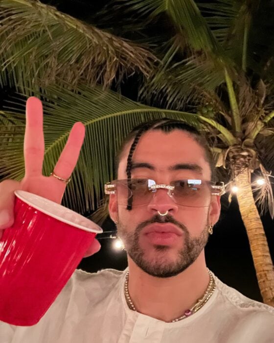 Selfie del cantante puertorriqueño Bad Bunny con la seña de amor y paz mientras sostiene un vaso rojo en la mano 