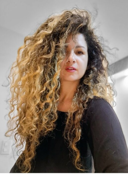 Selfie of a woman dressed in black with curly hair in blonde color with coffee 