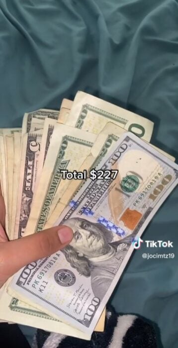 mano de una persona sosteniendo dólares bajo el texto de total $227 