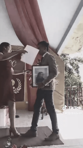 foto muestra a un chico subiendo al estrado a recibir su certificado abrazando la foto de su madre fallecida 