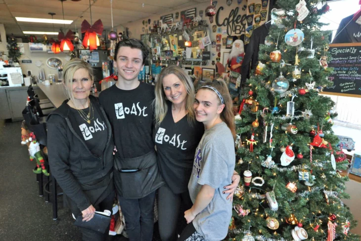 empleados uniformados de un restaurante sonríen a la cámara a un lado de ellos está un gran árbol de Navidad llevan ropa informal oscura