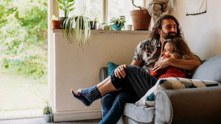 un hombre conforta con un abrazo a una mujer están sentados en un sillón 