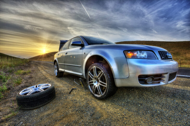 a gray car parked on the side of the road a spare tire is visible next to it it's getting dark