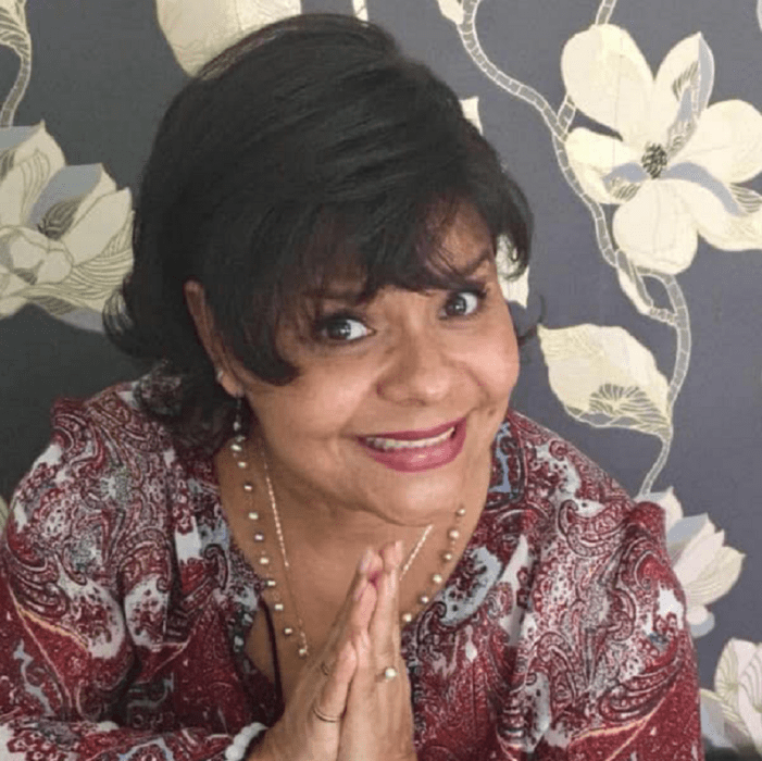 actress Claudia Ivette in a pose as if imploring wears a colorful patterned blouse wears little makeup